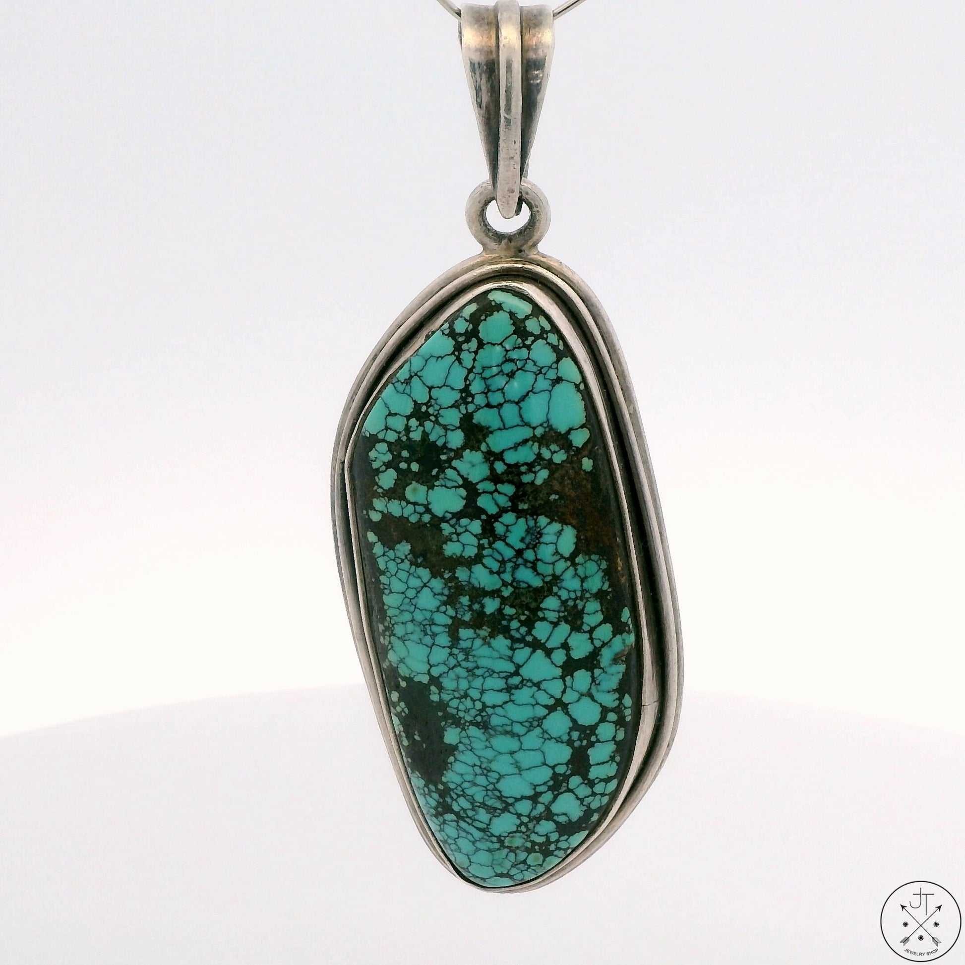 A sterling silver pendant with a large turquoise cabochon bale, featuring a vibrant blueish-green color with earthy tones.