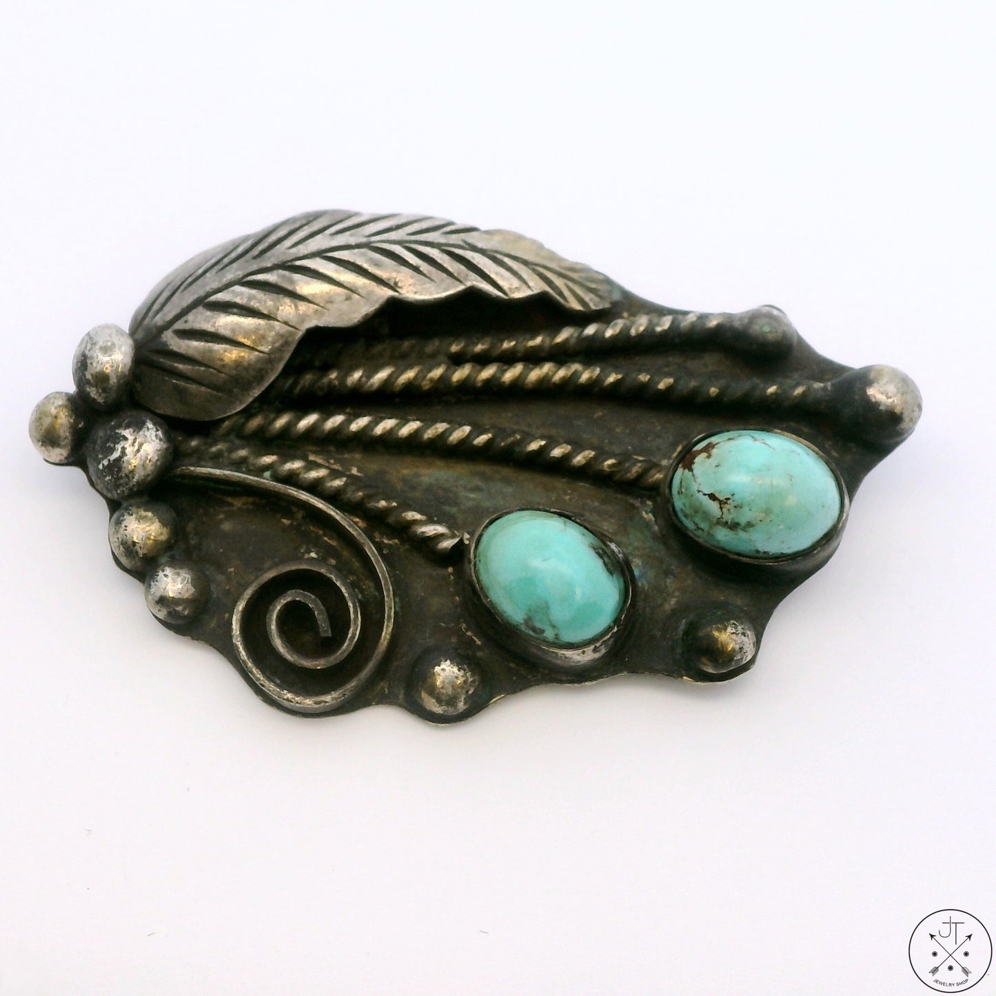 A vintage sterling silver leaf-shaped brooch with two turquoise cabochons and intricate detailing, displayed against a white background.