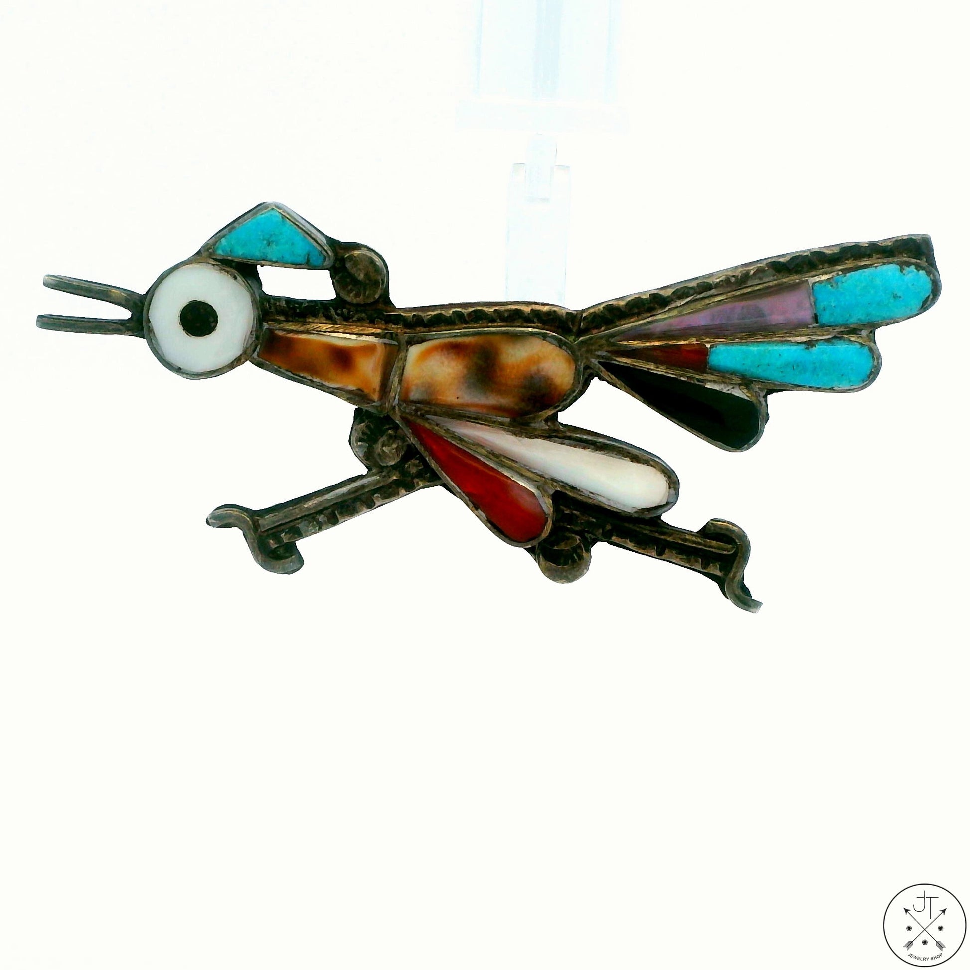 A vintage sterling silver brooch in the shape of a roadrunner bird with a dark patina finish, featuring colorful inlays of coral and turquoise.