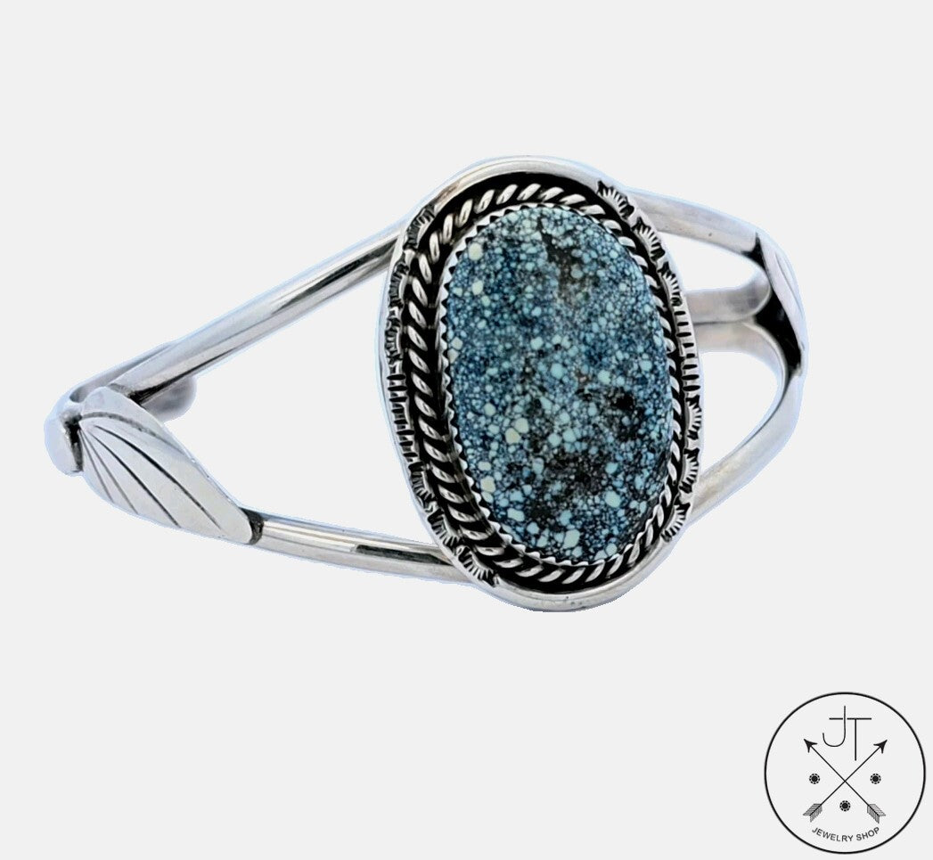 A vintage Navajo sterling silver cuff bracelet with a turquoise cabochon centerpiece surrounded by spider-webbing and geometric patterns.