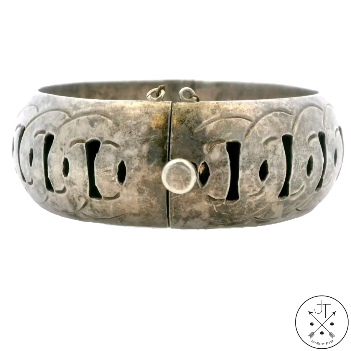 A vintage sterling silver hinged bangle bracelet with a safety chain, displaying etched patterns and an aged silver finish.