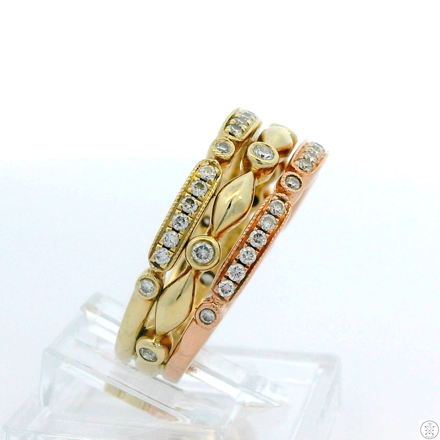 A stack of three 14k gold bands, two yellow and one rose, with intricate detailing and embedded sparkling diamonds.