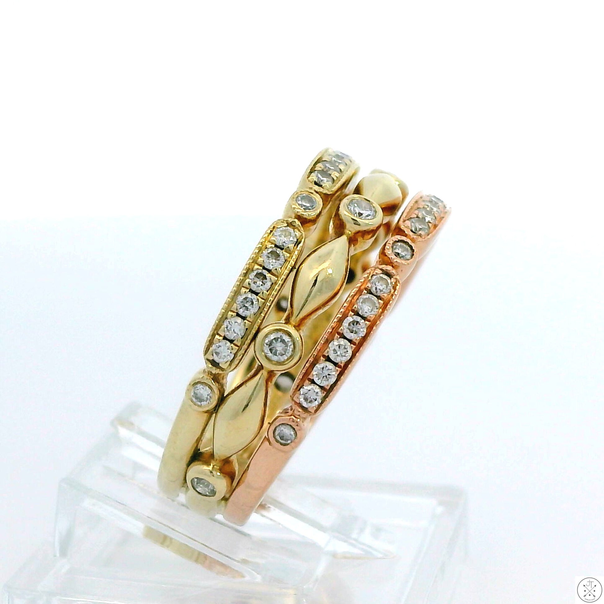 A stack of three 14k gold bands, two yellow and one rose, with intricate detailing and embedded sparkling diamonds.