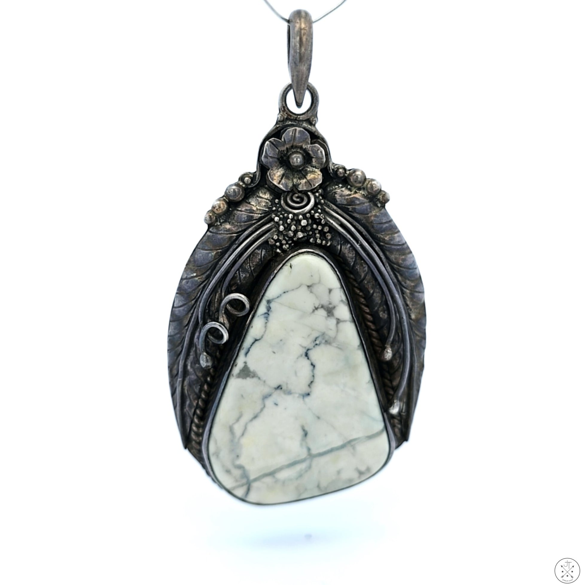 A vintage sterling silver pendant featuring a large white buffalo cabochon with a floral and leaves mounting, viewed against a neutral background.