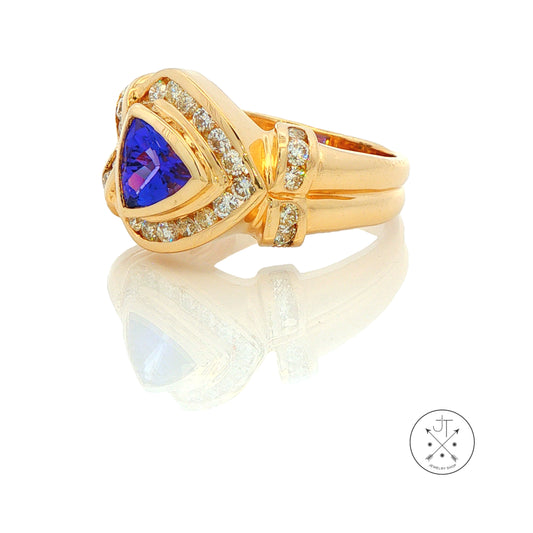 A yellow gold ring featuring a triangular blue gemstone center surrounded by small clear stones, shown on a white reflective background.