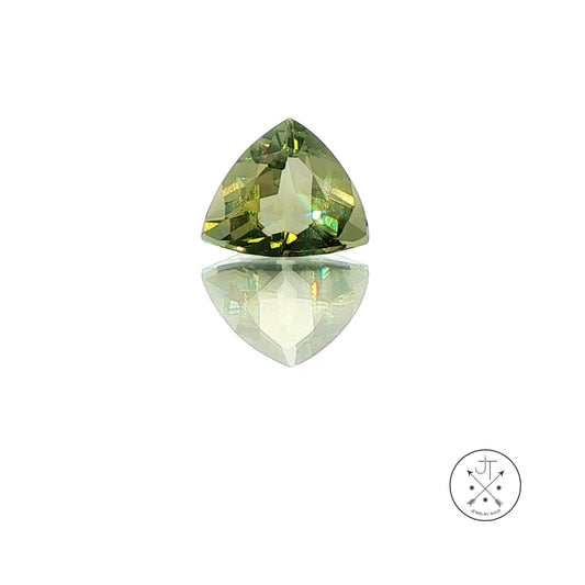 A single triangular faceted beryl gemstone in olive green with yellow-green and gold reflections, displayed on a reflective white surface against a white background, with a small circular logo in the bottom right corner.