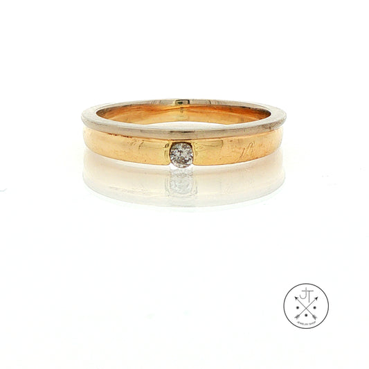 A two-tone yellow gold ring with a small round-cut diamond displayed on a reflective white surface against a white background.