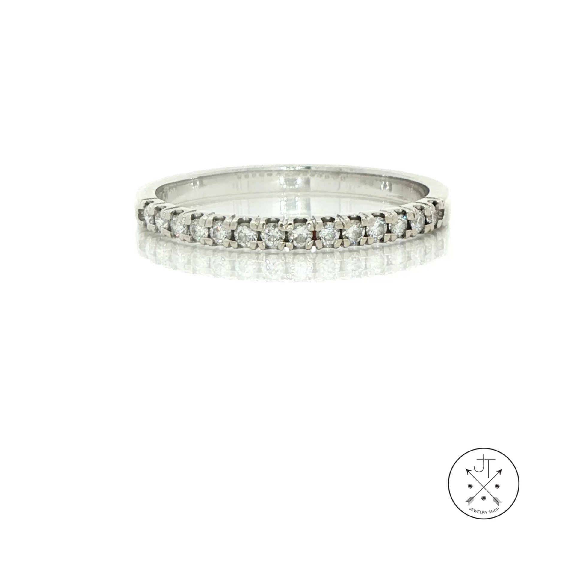 A silver diamond eternity ring with a continuous row of round-cut diamonds set in a polished white gold band, displayed on a reflective white surface against a white background.