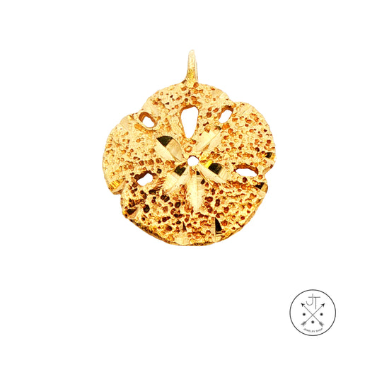 A textured gold sand dollar pendant with a central star motif and cutout details, shown on a plain white background with a small circular brand logo in the bottom right corner.