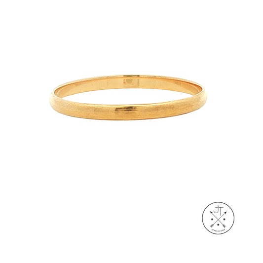 A thin, polished gold wedding band shown against a plain white background, with a small circular logo in the bottom right corner.