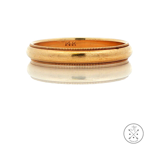 A vintage yellow gold band ring with a textured milgrain outer edge and a smooth inner band, displayed on a reflective white surface. The inside of the ring is stamped with '14K'.