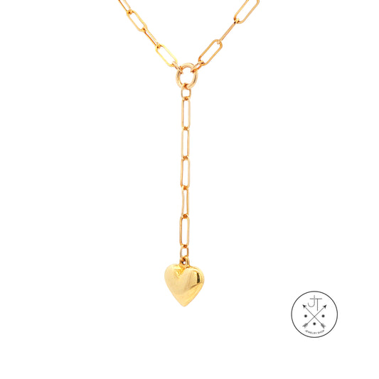 A gold paperclip chain necklace with a Y-shaped drop and a small heart pendant, shown on a plain white background with a circular brand logo in the bottom right corner.