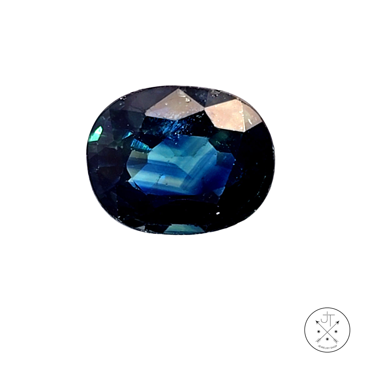 A faceted oval Sapphire gemstone with a deep blue color identity, showing iridescent blue and green reflections, isolated on a white background with a small logo in the bottom right corner.