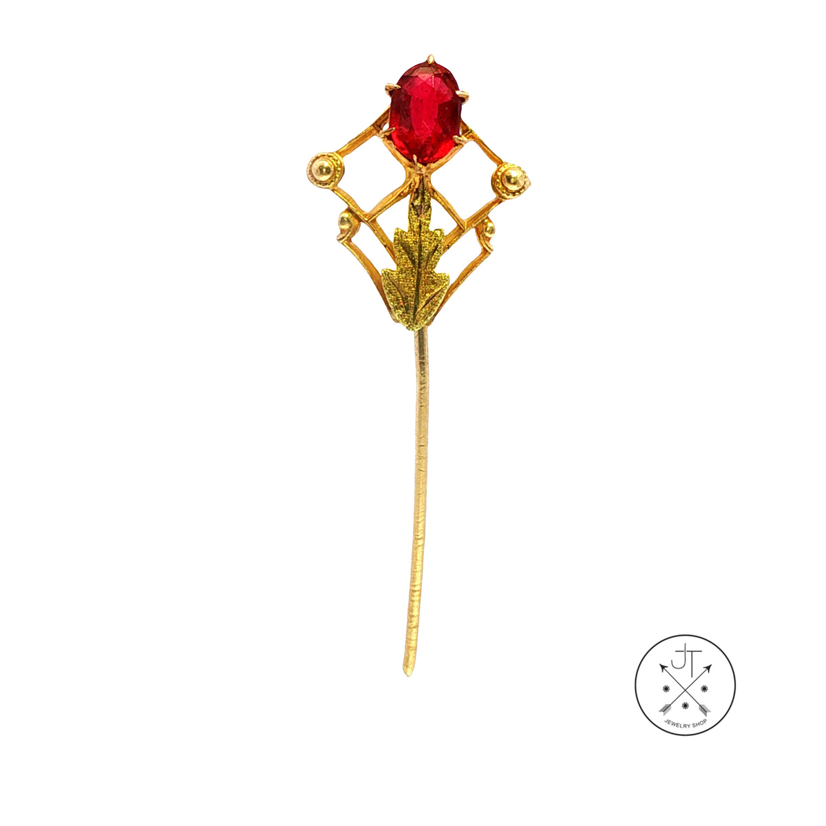 An antique gold brooch featuring an oval red gemstone in a geometric diamond-shaped setting with a long pin stem, shown on a plain white background with a small circular logo in the bottom right corner.