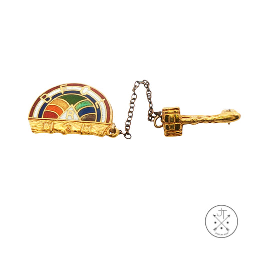 A gold vintage brooch featuring a colorful enamel rainbow arch over the left half and a textured gold chain leading to a gold gavel pin on the right, shown on a plain white background.