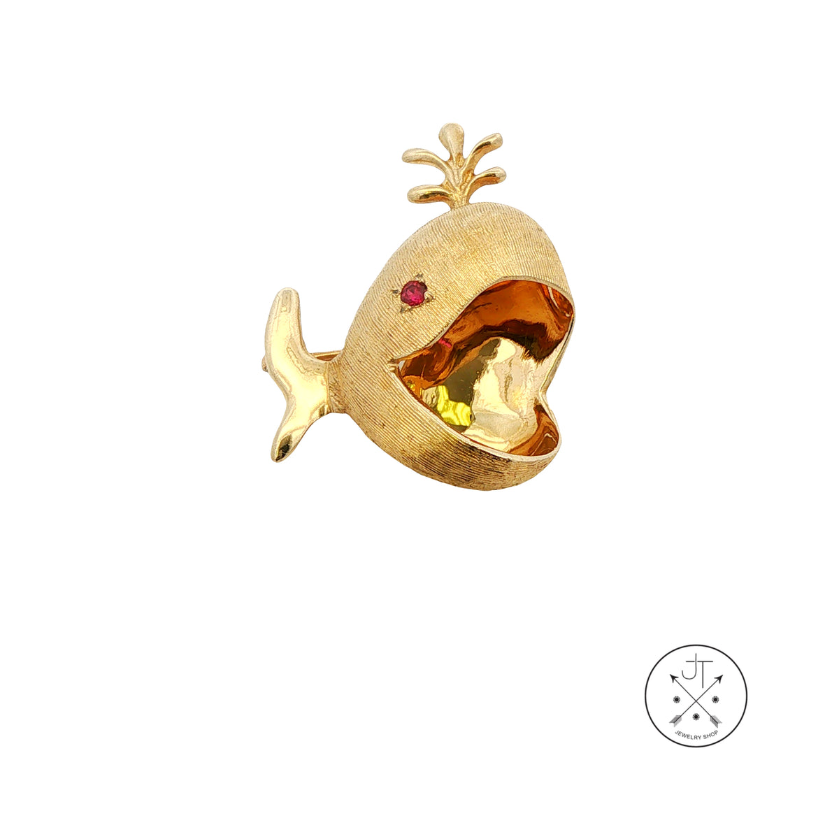 A gold whale-shaped brooch with an open mouth, featuring a small red gemstone eye, shown on a plain white background with a circular brand logo in the bottom right corner.